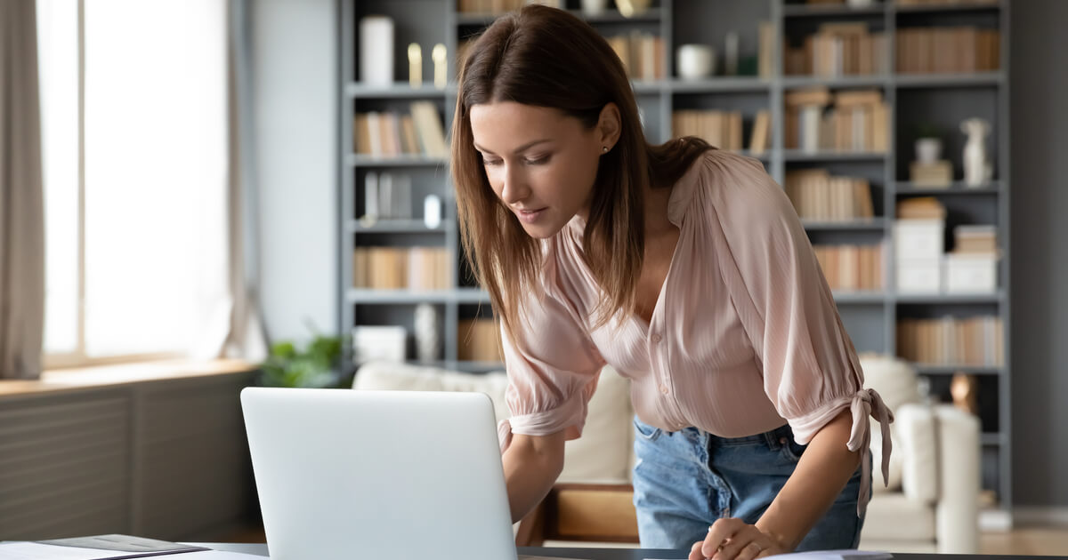 Junge Studentin arbeitet am Laptop und steht am Tisch.